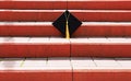 Black graduate cap with yellow tassel standing on bright orange steps of the stairs