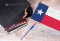 Black graduation hat on books next to Texas flag, education concept