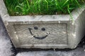 Black graffiti smile symbol on square grey concrete flower bed with green grass in it on the street of Moscow, Russia