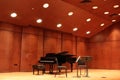 Black grand piano and bench with two chairs and music stands on light wood stage with medium wood walls and slanted ceiling lights Royalty Free Stock Photo