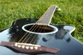 Black guitar lying on the green lawn with a focus on the strings