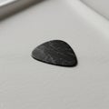 A black guitar pick with a marbled pattern, featuring a rounded triangular shape, lies o Royalty Free Stock Photo