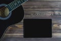 A black guitar and a black tablet screen on a brown wooden surface close-up. The concept of a layout for advertising online guitar Royalty Free Stock Photo