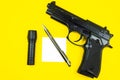 Black gun, reminder note paper, pen and flashlight lies on a yellow background. Private detectives work. Searching information