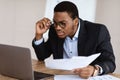Black guy with glasses accountant holding papers, using laptop