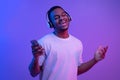 Black guy in headphones listening music on smartphone and singing, neon lighting