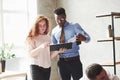 Black guy and redhead girl read the reports in the office with plants