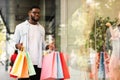 Black guy with shopping bags looking at shop window outdoors Royalty Free Stock Photo