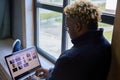 Black guy with glasses is sitting on the windowsill and using a laptop, working remotely, studying Royalty Free Stock Photo