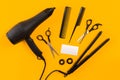 Black hair dryer, comb and scissors on yellow paper background. Top view Royalty Free Stock Photo