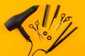 Black hair dryer, comb and scissors on yellow paper background. Top view Royalty Free Stock Photo