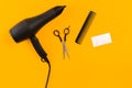 Black hair dryer, comb and scissors on yellow paper background. Top view Royalty Free Stock Photo