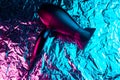 Black hair dryer in neon lights on the foil with shiny crumpled surface background.