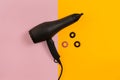 Black hair dryer on pink and yellow paper background. Top view Royalty Free Stock Photo