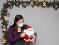 Black hair latin woman with protection mask and santaclaus doll in christmas decoration, new normal covid-19