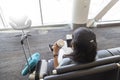 Black-haired Caucasian woman is sitting in an airport lounge seat with her passport and a coffee in her hands. She also has her