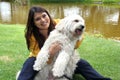 black haired latin woman sitting on outdoor park lawn with her white dog breed Labradoodle