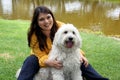 Black haired latin woman sitting on outdoor park lawn with her white dog breed Labradoodle