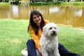 Black haired latin woman sitting on outdoor park lawn with her white dog breed Labradoodle