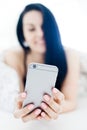 Black haired sexy woman relaxing and using silver cell phone on bed Royalty Free Stock Photo