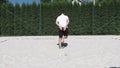 Black-haired, sinewy athlete warms up before a match on a beach volleyball court. Athlete shows stumbling, backward kick