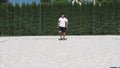 Black-haired, sinewy athlete warms up before a match on a beach volleyball court. Athlete demonstrates running with knee lifts