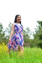 A black-haired woman wearing blue flowery summer dress standing in the green meadow Royalty Free Stock Photo