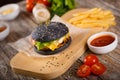 Black hamburger with bacon and sauce on a wooden stand