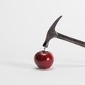 Black hammer hitting a nail on red apple on white background