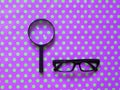 Black Hand-Held Reading Magnifier, Magnifying Glass, a Pair of Glasses on fluorescent purple green spotted pattern background.