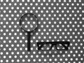 Black Hand-Held Reading Magnifier, Magnifying Glass, a Pair of Glasses on grey and white spotted pattern background.