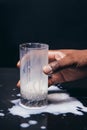 Black hand hold glass, spill white milk on table