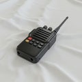 A black handheld walkie-talkie with an antenna is placed on a smooth, white fabric Royalty Free Stock Photo