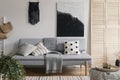 Black handmade macrame above grey comfortable couch with pillows and warm blanket, real photo with mockup on the empty wall