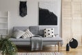 Black handmade macrame and fancy painting on white wall of sophisticated living room interior with grey fashionable couch with