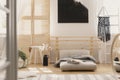 Black handmade macrame on white wooden ladder in bright bedroom interior with wooden furniture and beige futon with grey warm