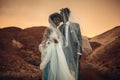 Newlyweds stand under bridal veil, smile and kiss in canyon at sunset.