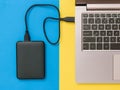 Black hard drive and laptop on yellow and blue background. Flat lay. The concept of backup storage