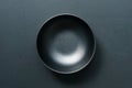 On a black hardwood background, a top view of a black empty round ceramic bowl