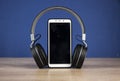 Black headphones and smart phone with stack books on wooden table againts blue wall Royalty Free Stock Photo