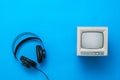 Black headphones with wire and a small retro monitor on a blue background.