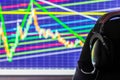 Black headset on chair over monitor with trading chart in background - dark background with selective focus Royalty Free Stock Photo