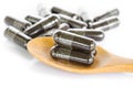 Black herbal capsule drug in wooden spoon.