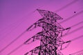 Black high-voltage poles and electric power transmission lines are connected from a power plant on an isolated purple-pink Royalty Free Stock Photo