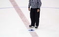 Black hockey puck and referee legs on ice rink. Winter sport Royalty Free Stock Photo