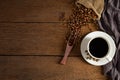 Black hot fresh coffee in a white ceramic cup with coffee beans roasted in burlap sack bag on wooden table background. Royalty Free Stock Photo