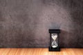 Black hourglass on a wooden table with old gray concrete walls. Royalty Free Stock Photo