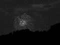 Fireworks explode over nightsky hillside monochrome.