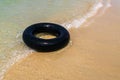 A Black inflatable donut on the seashore. with soft wave of blue ocean in outdoor sun lighting on sandy beach.