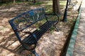 A black iron bench placed in a shady park area beside Royalty Free Stock Photo
